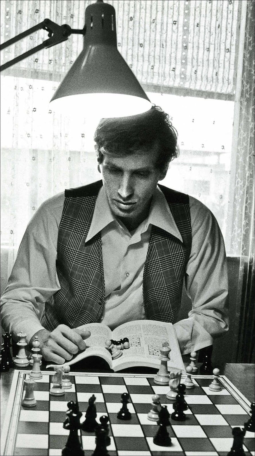 Bobby Fischer studying chess openings with a book and board in a vintage black and white photograph HD phone wallpaper