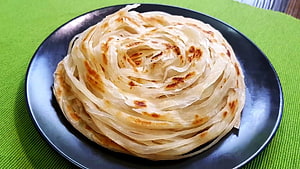 Flaky Layered Parotta Served on a Dark Plate with Golden Brown Spots HD wallpaper