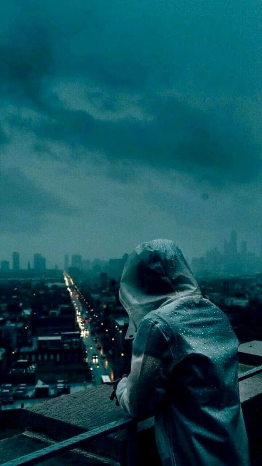 Lone figure in a rain-soaked hood overlooking a moody city skyline at dusk HD phone wallpaper