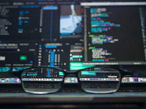 Cybersecurity Analyst Workspace with Code on Screen and Glasses HD wallpaper