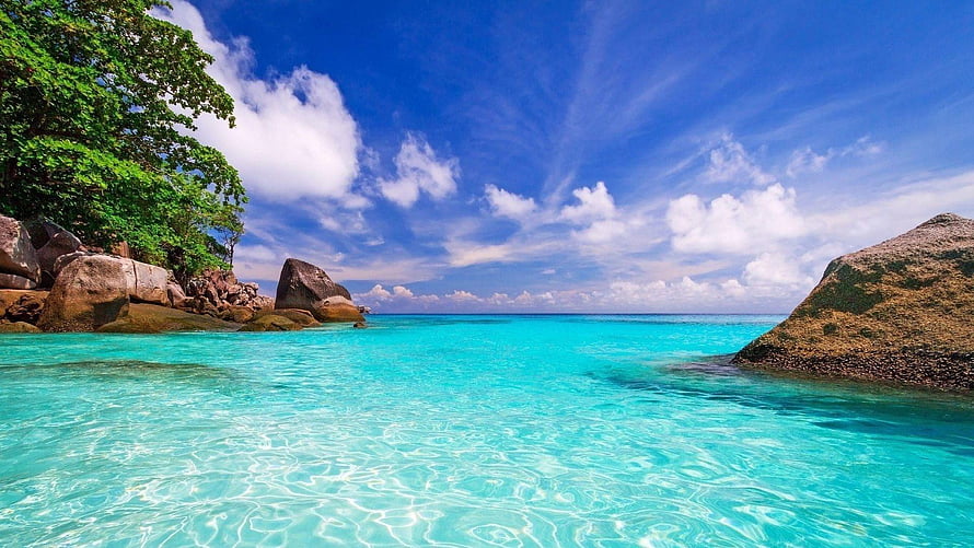 Turquoise tropical lagoon with granite boulders and lush green trees under a bright blue sky HD wallpaper