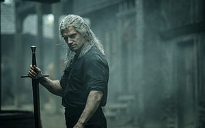 Henry Cavill as Geralt of Rivia holding a sword in a dim stone corridor from The Witcher HD wallpaper
