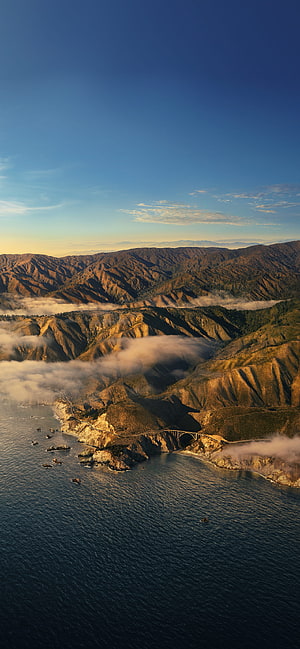 Aerial View of Coastal Highway Bridge Overlooking Ocean and Mountain Valleys at Golden Hour HD phone wallpaper