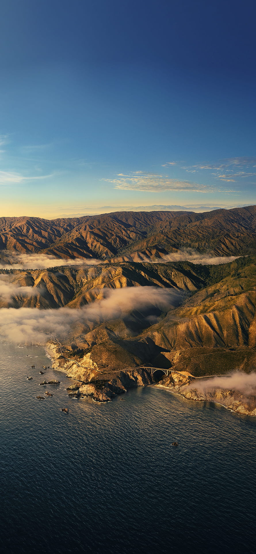 Aerial View of Coastal Highway Bridge Overlooking Ocean and Mountain Valleys at Golden Hour HD phone wallpaper