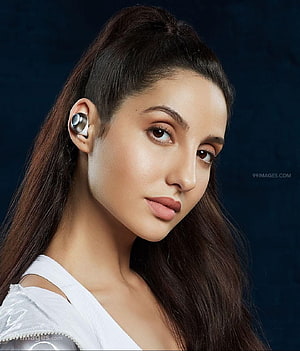 Nora Fatehi Wearing Wireless Earbuds in a White Top Against a Dark Blue Background HD phone wallpaper