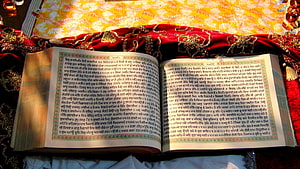 Open Guru Granth Sahib scripture resting on ornate red and gold ceremonial cloth HD wallpaper