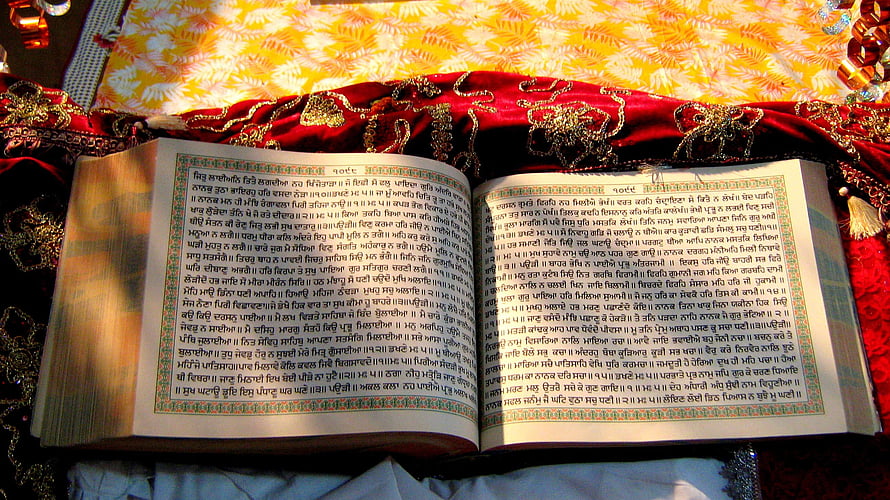 Open Guru Granth Sahib scripture resting on ornate red and gold ceremonial cloth HD wallpaper