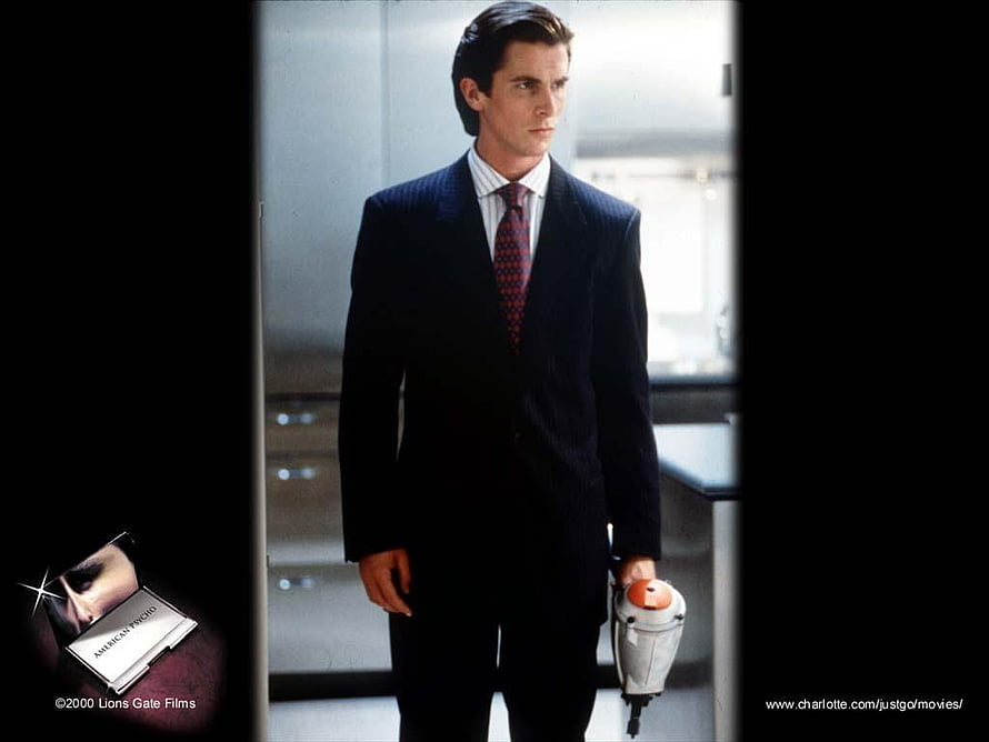 Patrick Bateman in a dark suit holding a weapon in the American Psycho film scene HD wallpaper