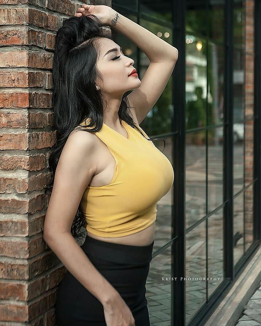 Young woman in yellow crop top leaning against brick wall with long dark hair HD phone wallpaper