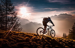 Mountain Biker Silhouette on Alpine Ridge at Golden Hour Sunset HD wallpaper