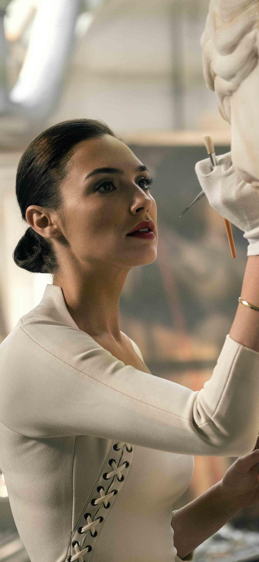 Gal Gadot as Wonder Woman in a white lace-up bodysuit holding a paintbrush in a studio setting HD phone wallpaper