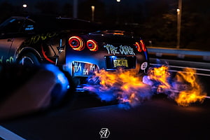 Nissan GT-R with Joker livery performing a fiery burnout on a dark highway at night HD wallpaper