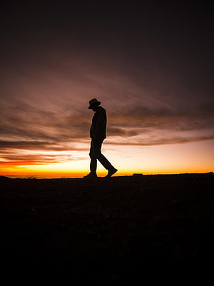 Silhouette of a man in a hat walking along a dark ridge at sunset HD phone wallpaper