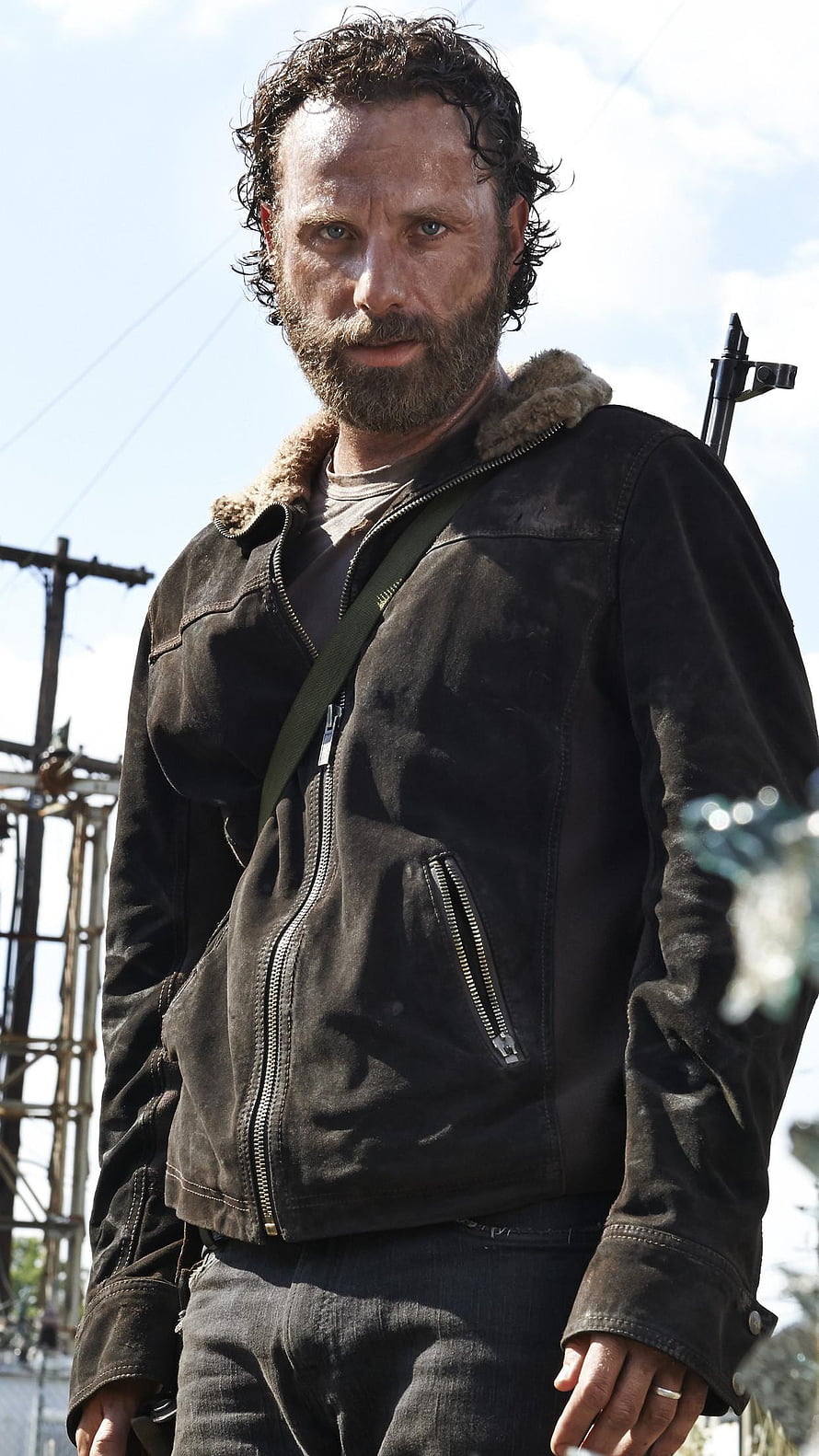 Rick Grimes in a worn leather jacket with a crossbow slung over his shoulder in a post-apocalyptic setting HD phone wallpaper