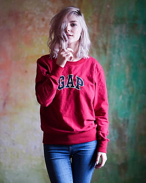 Eva Elfie in a red Gap sweatshirt and blue jeans against a colorful textured wall HD phone wallpaper
