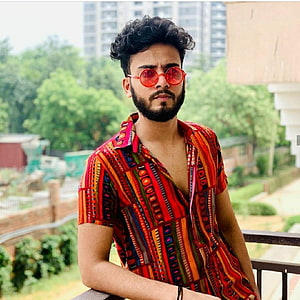 Elvish Yadav in a vibrant patterned shirt and red sunglasses on a balcony HD phone wallpaper