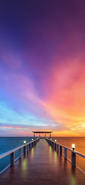 Illuminated Pier Extending Into Calm Ocean Under Vibrant Sunset Sky HD phone wallpaper