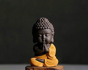Cute Chibi Buddha Statue in Yellow Robe with Praying Hands on Wooden Base HD wallpaper