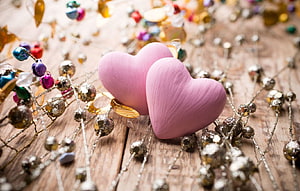 Two pink ceramic hearts resting on rustic wood surrounded by colorful beaded jewelry and festive decorations HD wallpaper