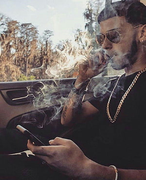 Anuel AA Smoking Cigar in Car with Gold Chain and Aviator Sunglasses HD phone wallpaper