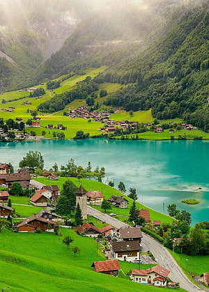 Lake Lungern in the Canton of Obwalden, Switzerland, framed by lush green alpine hills and traditional village houses HD phone wallpaper