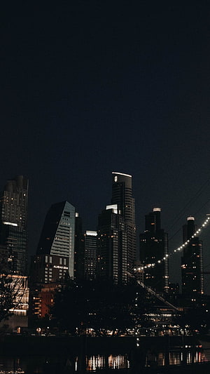 Moody Urban Skyline at Night with Illuminated High-Rise Buildings and Water Reflections HD phone wallpaper