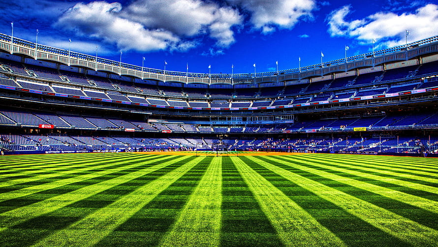 Vibrant Green Football Pitch Inside a Large Multi-Tiered Stadium Under a Blue Sky HD wallpaper