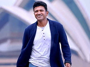 Puneeth Rajkumar in a navy blazer and white henley shirt with a modern architectural backdrop HD wallpaper