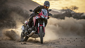 Rider on a Red Honda Africa Twin Adventure Motorcycle Kicking Up Dust on a Desert Trail at Sunset HD wallpaper