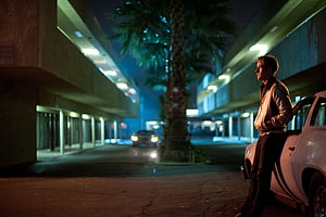 Ryan Gosling in Drive leaning against a white car in a neon-lit parking lot at night HD wallpaper