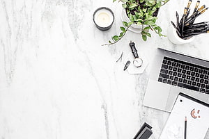 Minimalist White Marble Workspace With Laptop, Plant, And Candle HD wallpaper