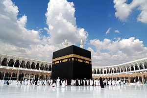 The Sacred Kaaba in Mecca with Pilgrims Performing Tawaf Under a Bright Blue Sky HD wallpaper