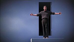 The Truman Show cinematic still of a man standing on a platform with arms outstretched against a blue wall HD wallpaper