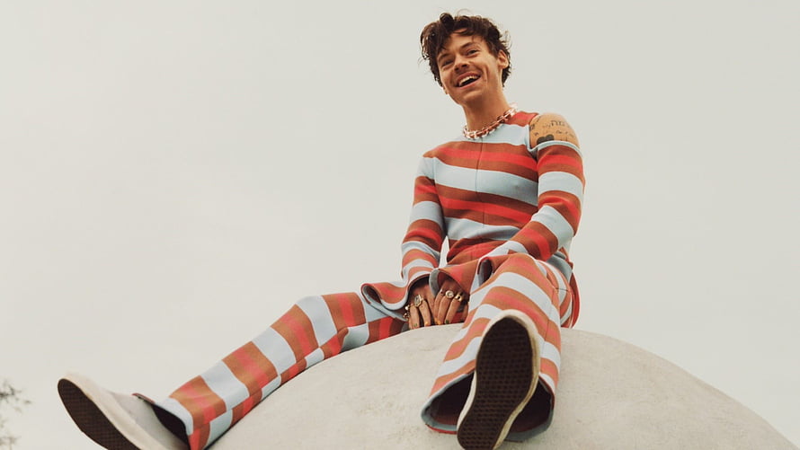 Harry Styles in a red and white striped suit sitting on a curved white surface HD wallpaper