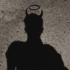 Dark silhouette of a horned figure with a halo against a textured concrete wall HD phone wallpaper