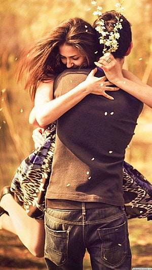 Romantic couple embracing in a golden field with white flowers HD phone wallpaper