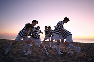 ENHYPEN members in striped sweaters and white shorts dancing on a beach at sunset HD wallpaper
