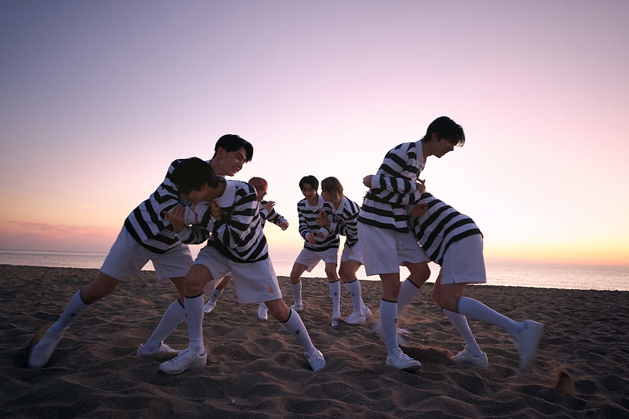 ENHYPEN members in striped sweaters and white shorts dancing on a beach at sunset HD wallpaper