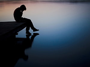 Silhouette of a solitary figure sitting on a dock at dusk with a calm water reflection HD wallpaper