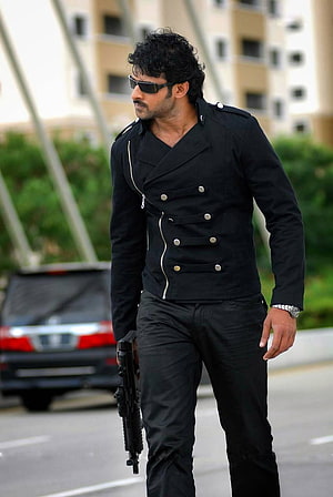 Prabhas as Billa in a black military-style jacket and sunglasses holding a rifle HD phone wallpaper