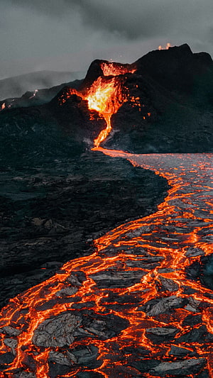 Molten Lava Flowing Down a Dark Volcanic Slope Under a Stormy Sky HD phone wallpaper