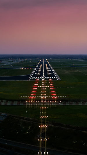 Aerial View of Airport Runway at Dusk with Glowing Approach Lights and Pink Twilight Sky HD phone wallpaper