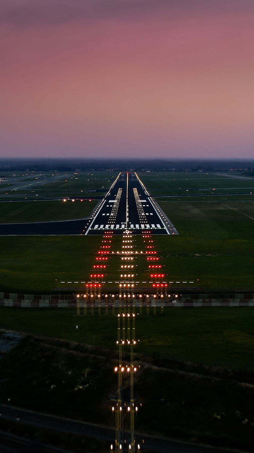 Aerial View of Airport Runway at Dusk with Glowing Approach Lights and Pink Twilight Sky HD phone wallpaper
