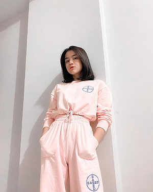 Young Woman in Pastel Pink Sweatpants and Crewneck Sweatshirt Leaning Against White Wall HD phone wallpaper