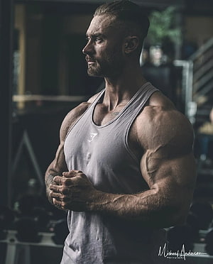 Muscular Man in Grey Tank Top Standing in Dark Gym with Dramatic Lighting HD phone wallpaper