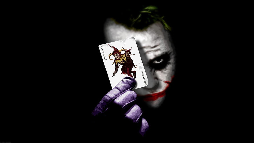 The Joker holding a playing card in dark cinematic lighting HD wallpaper