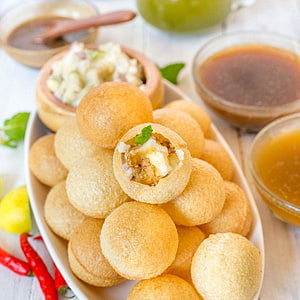 Golden Pani Puri Stuffed with Spiced Potato and Fresh Mint on a White Platter HD phone wallpaper