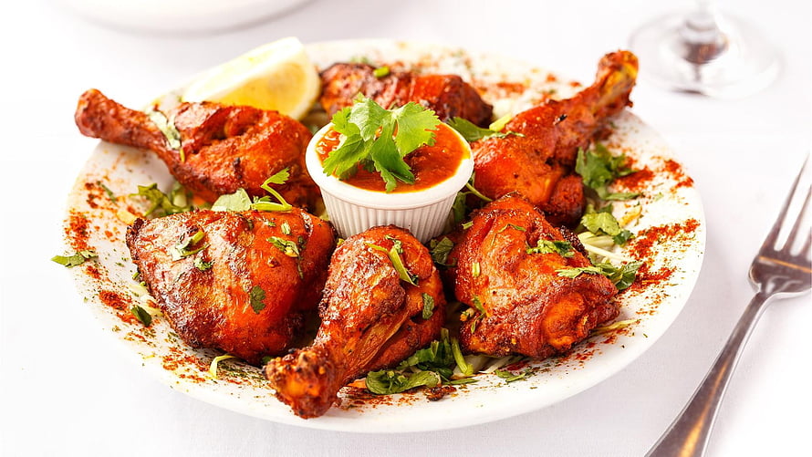 Spiced grilled chicken legs with fresh cilantro and dipping sauce on a white plate HD wallpaper