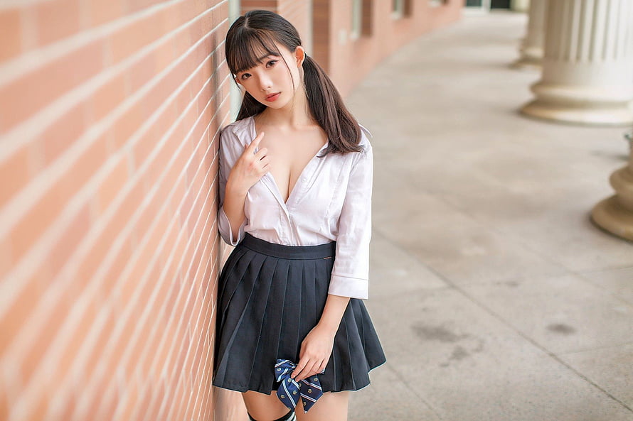 Young Asian woman in white blouse and pleated skirt leaning against brick wall HD wallpaper