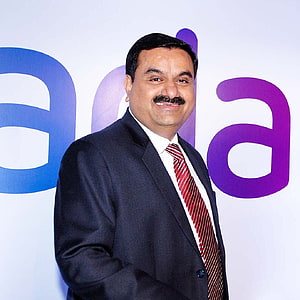 Gautam Adani in a dark suit and red striped tie standing before a corporate backdrop HD phone wallpaper